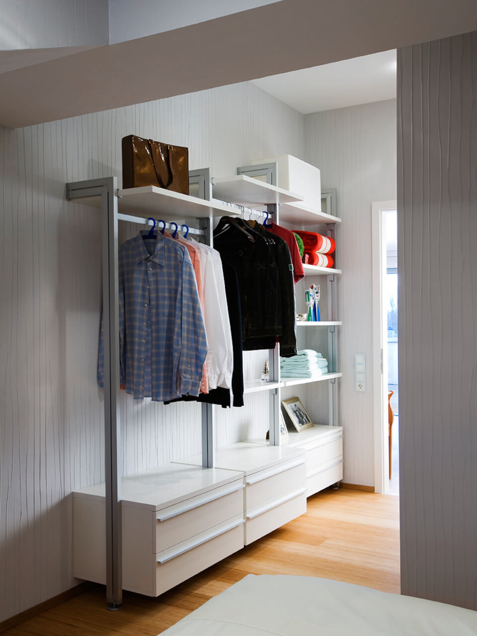 Kompaktes Schranksystem für Dachschrägen mit Hängemöglichkeit, Schubladen und offener Regalfläche in einer schmalen Nische