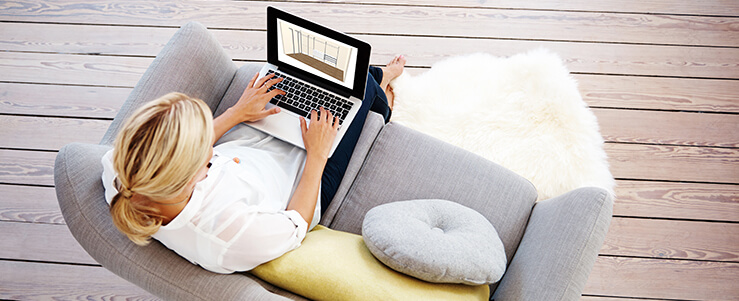 Eine Frau sitzt gemütlich auf einem Sofa mit einem Laptop auf den Beinen und plant ein Schranksystem von FRANK Schranksysteme im 3D Schrankplaner.