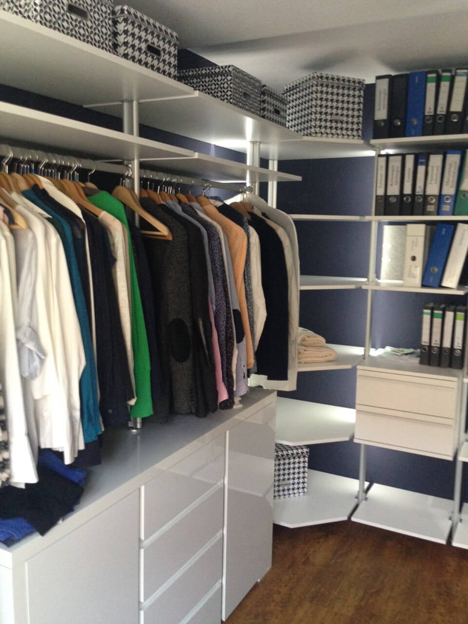 Offenes Schranksystem mit Kleidung, Boxen und Aktenordnern im begehbaren Kleiderschrank mit Ecklösung