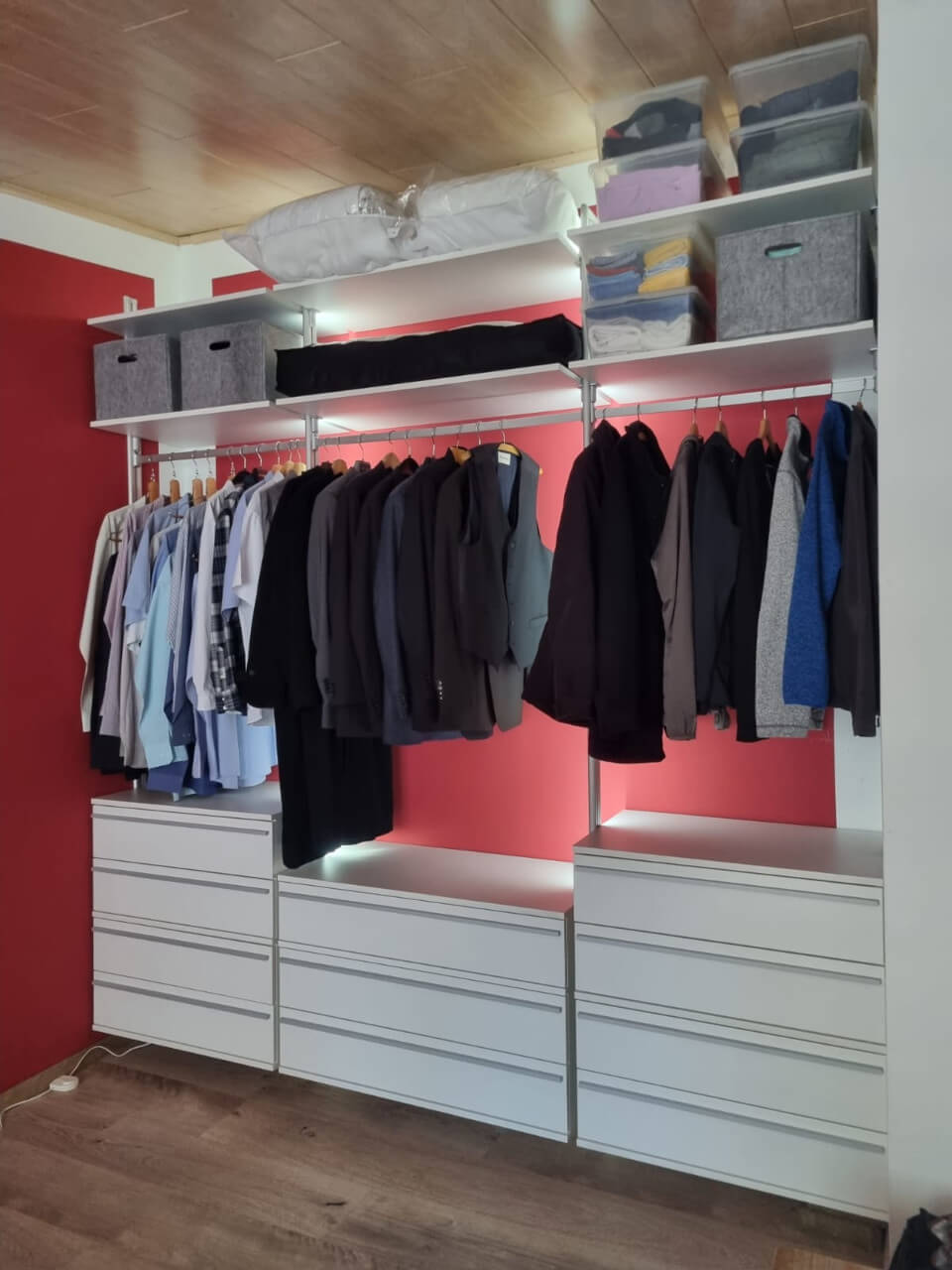 Offener Kleiderschrank mit integrierter LED vor roter Wand, Hemden und Anzügen, sowie vielen Schubladen