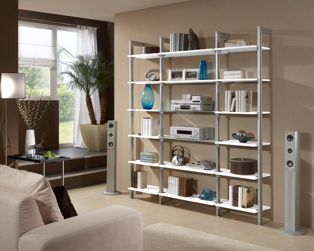 Ein Wohnzimmer mit einer gemütlichen Couch, die einladend und modern wirkt sowie einem Bücherregal mit 18 Glasböden nicht nur für Bücher auch für Multimedia Technik und ihre liebsten Accessoires.